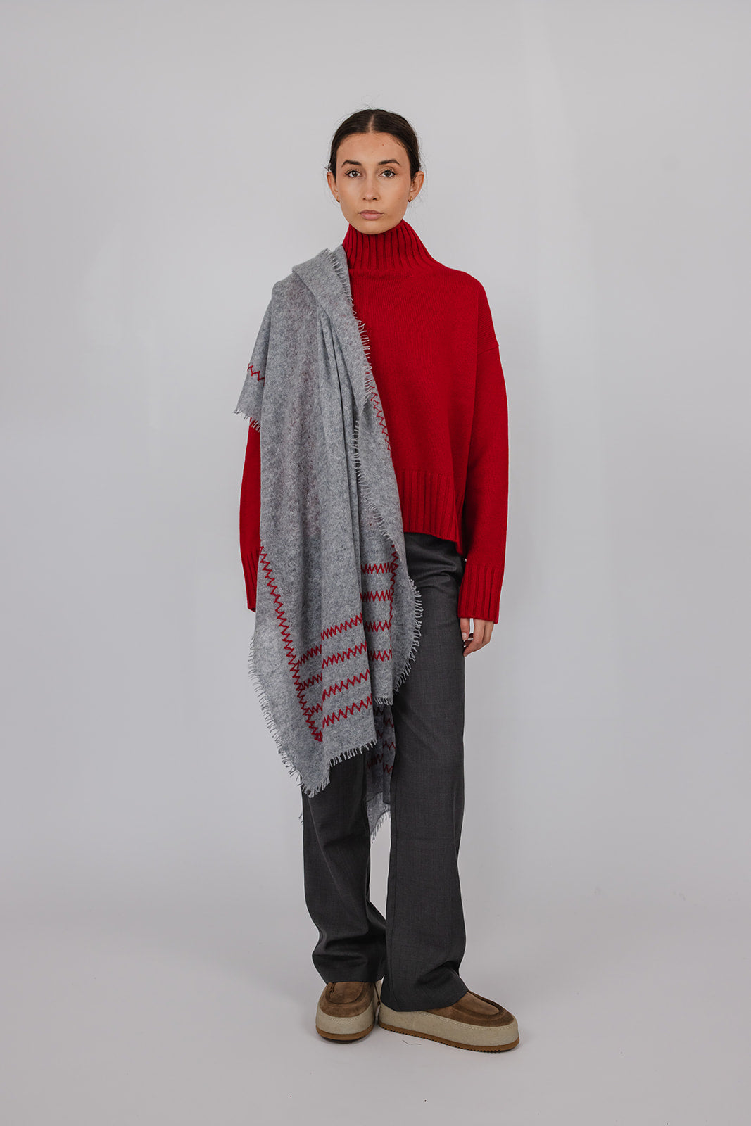 Model wearing a red funnel neck knit and grey suit pants with a grey cashmere scarf with red hand stitching detail by Vic and Bert.