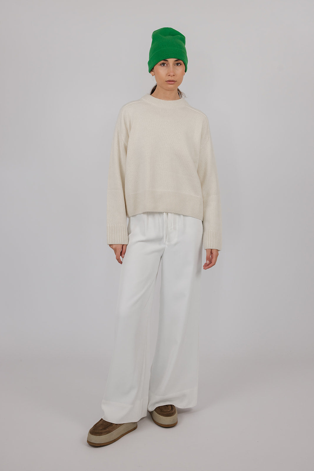 Model wearing a chalk coloured cashmere knit with white pants and a green cashmere beanie by Vic and Bert.