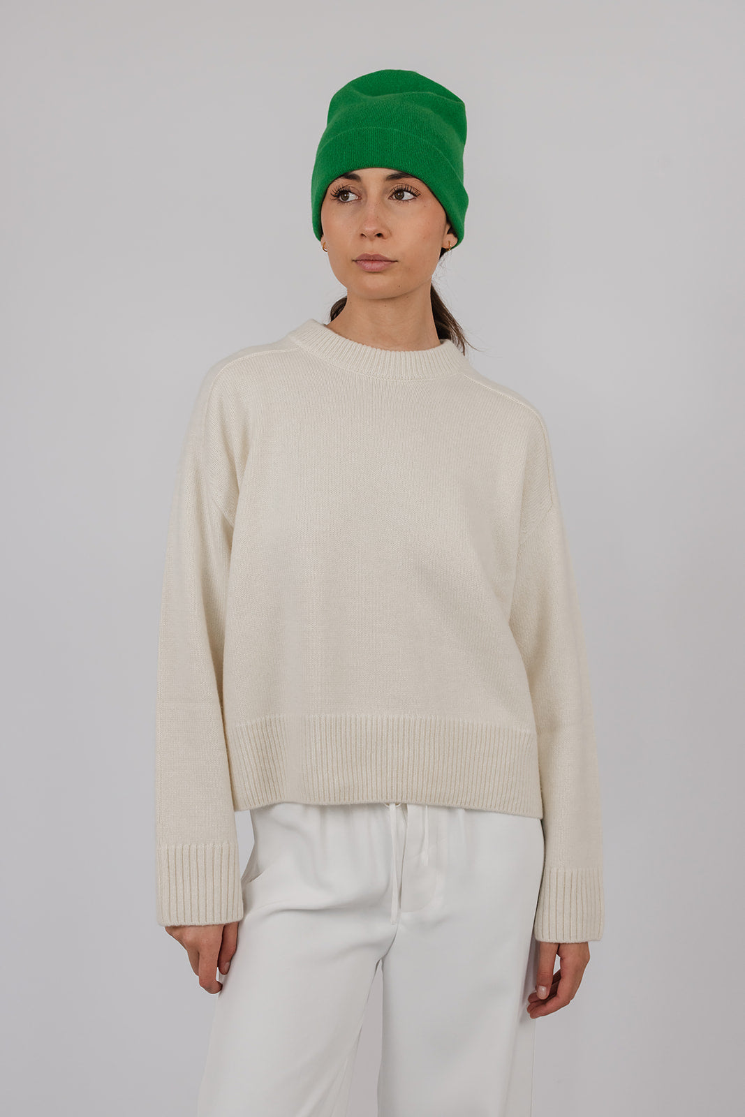 Model wearing a chalk coloured cashmere knit with white pants and a green cashmere beanie by Vic and Bert.
