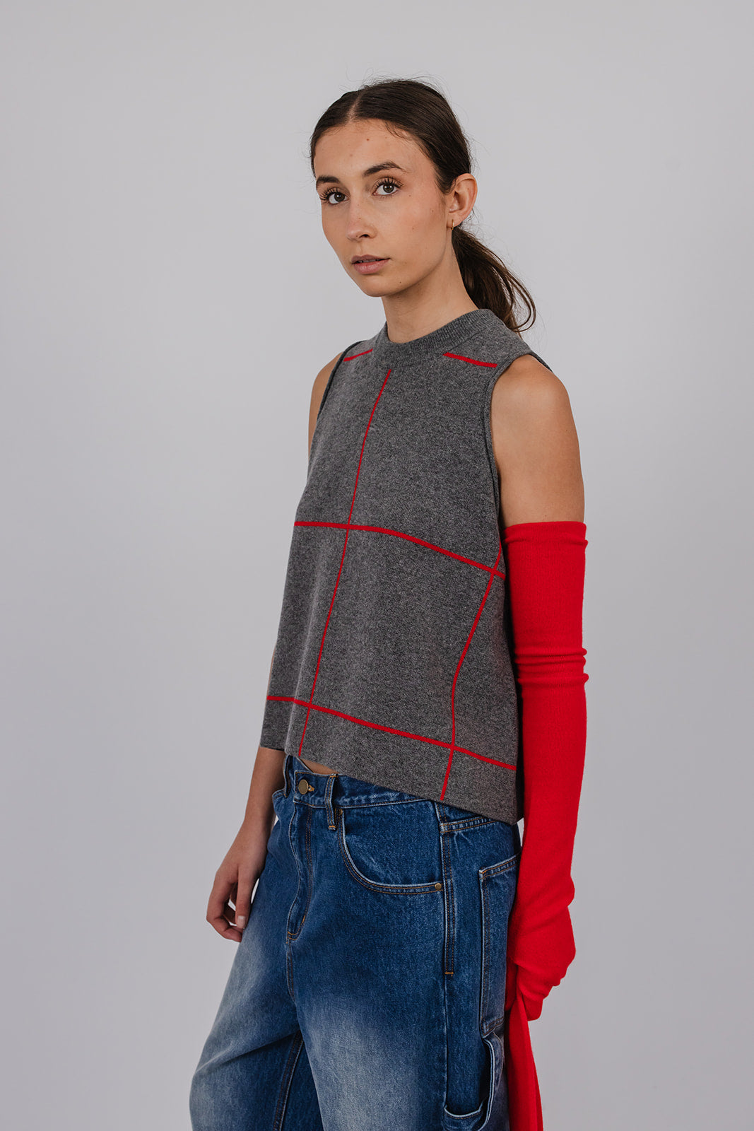 Model wearing a grey and red cashmere vest, blue carpenter jeans, and red cashmere gloves by Vic and Bert.