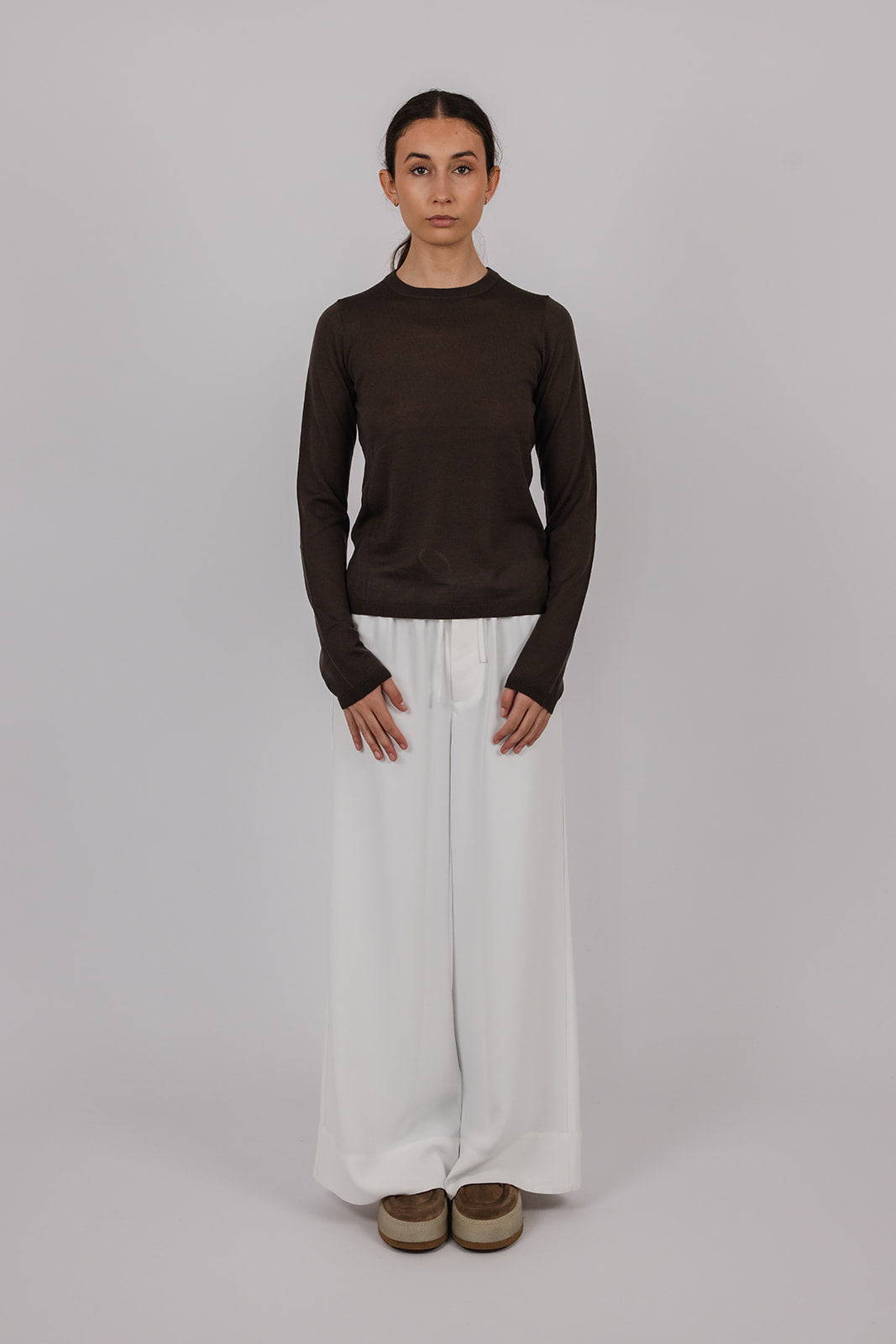 Model wearing a chocolate coloured long-sleeve merino top and white pants by Vic and Bert.
