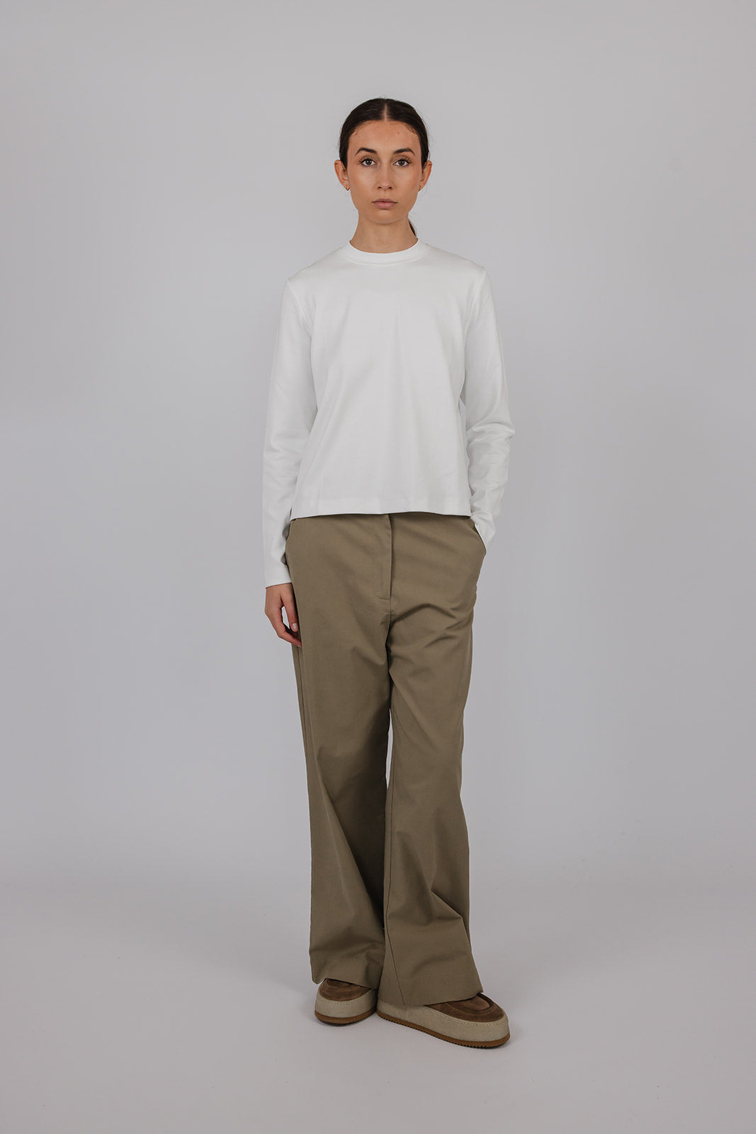 Model wearing a white thick long sleeve tee and green pants by Vic and Bert.
