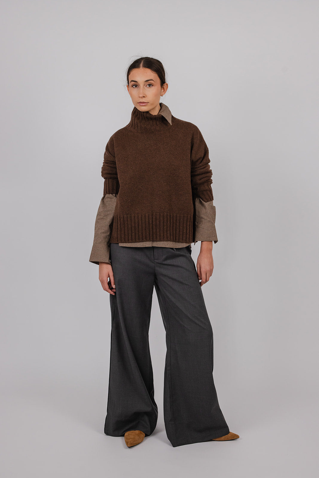 Model wearing a black tea coloured turtle neck knit over a brown shirt with grey suit pants by Vic and Bert.