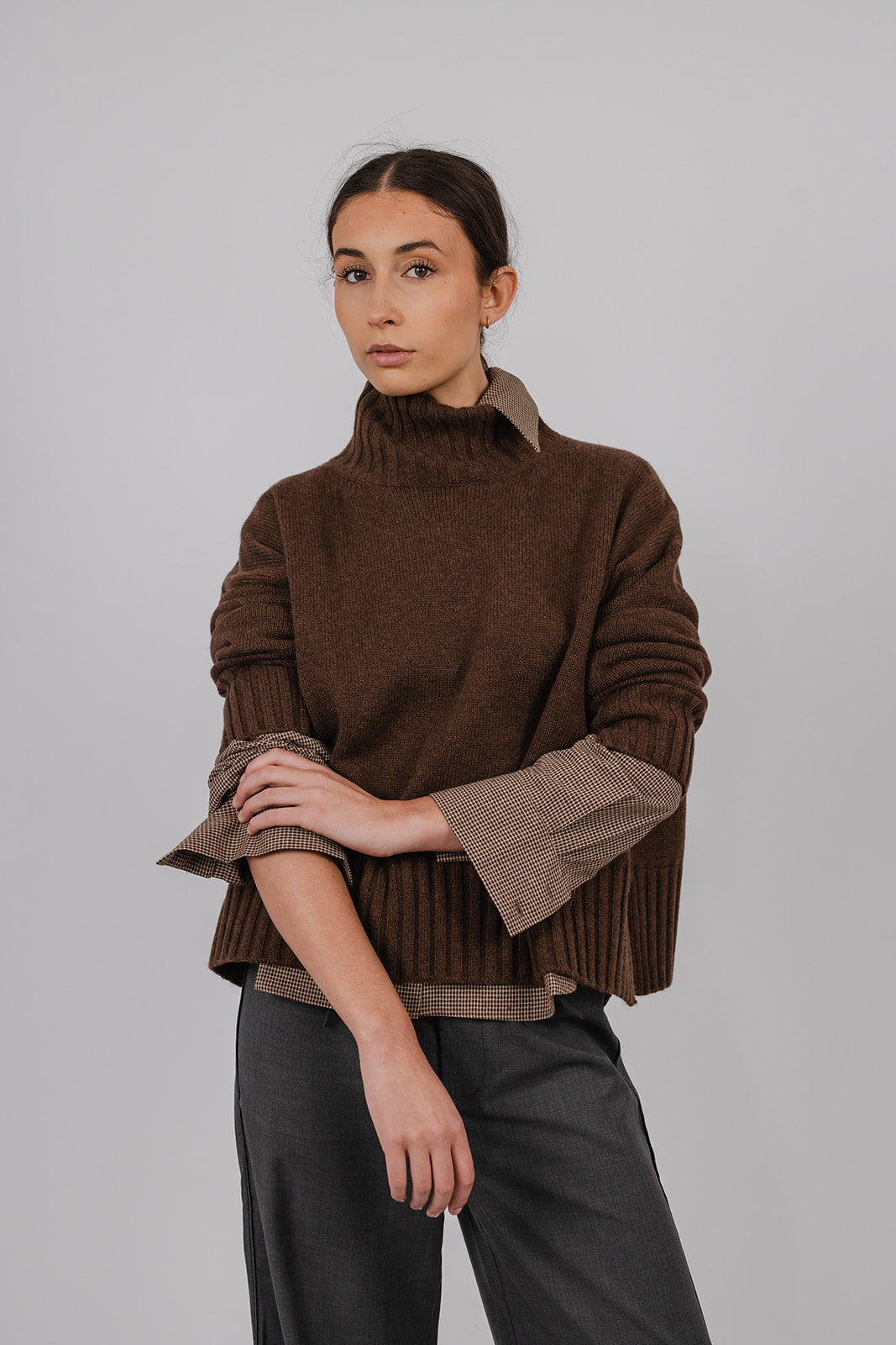 Model wearing a black tea coloured turtle neck knit over a brown shirt with grey suit pants by Vic and Bert.