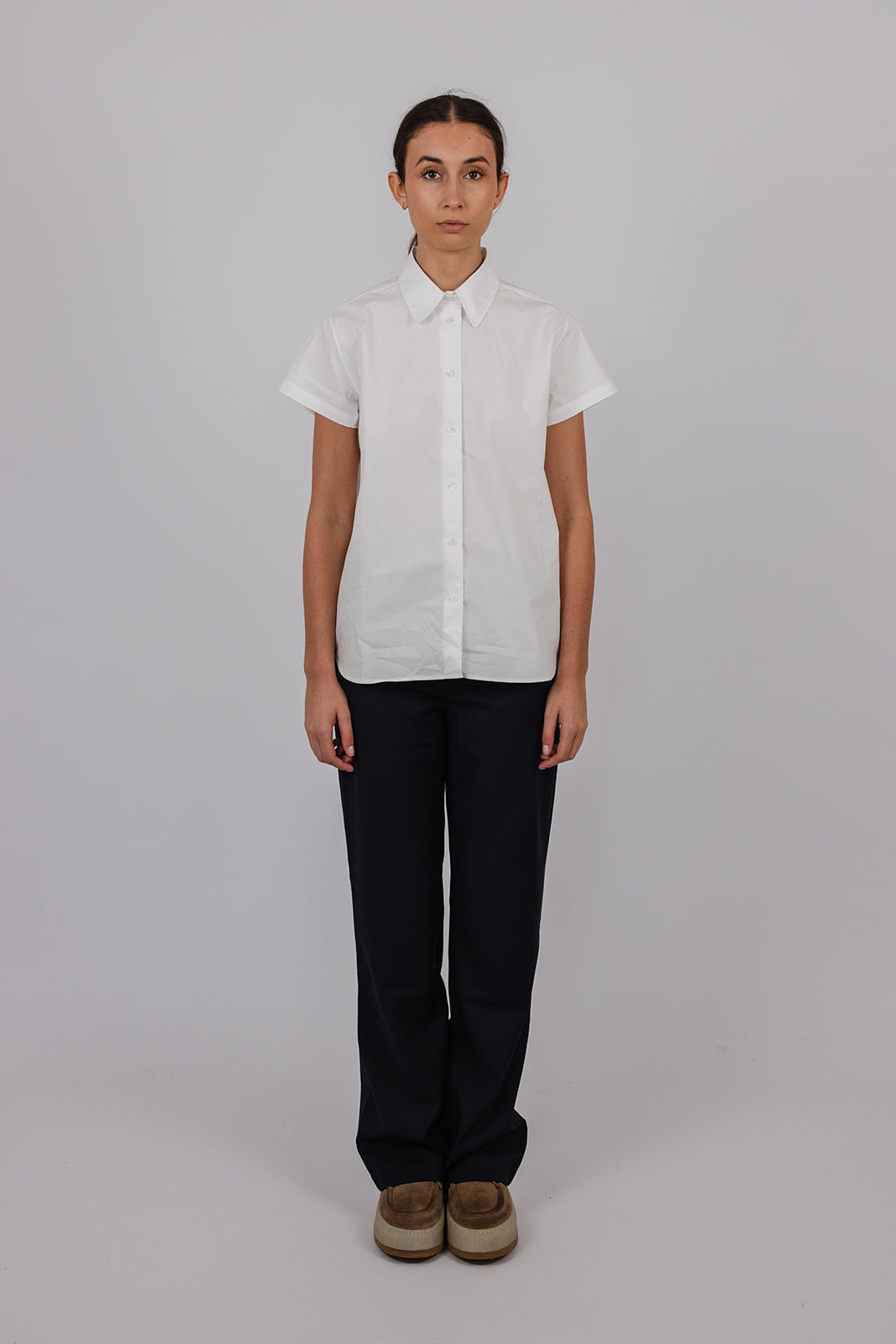 Model wearing a white short sleeve cotton collared shirt and navy suit pants by Vic and Bert.