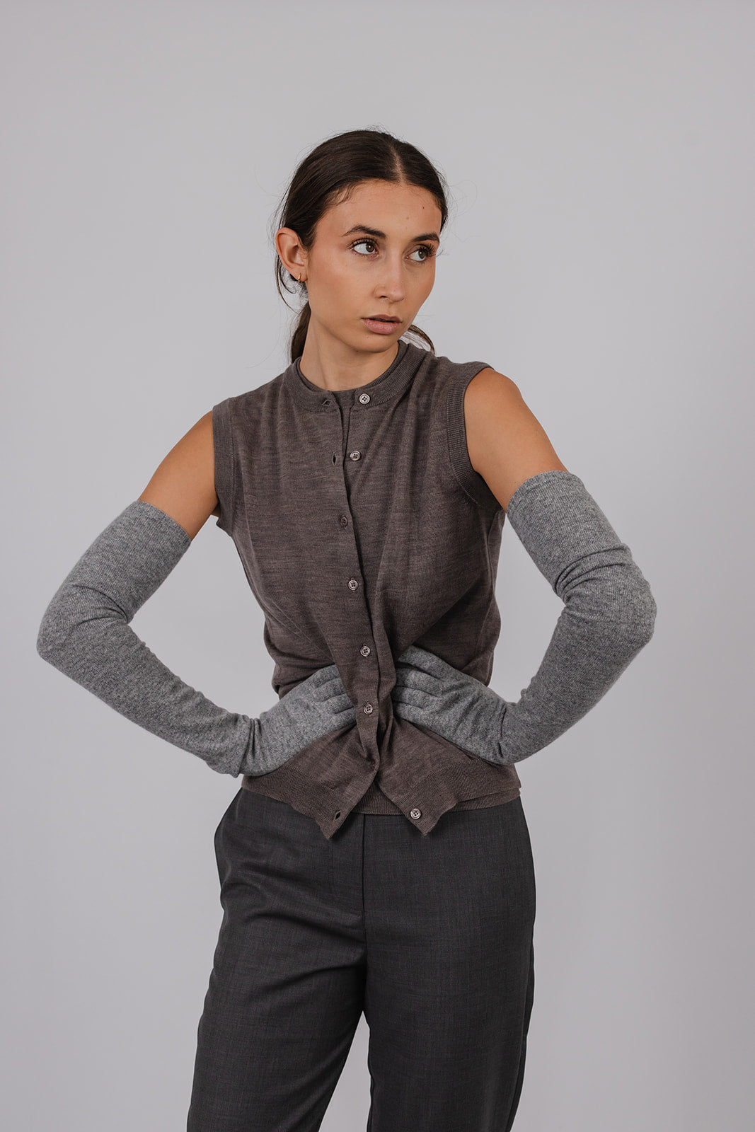 Model wearing a dark stone coloured sleeveless merino vest and grey suit pants by Vic and Bert.