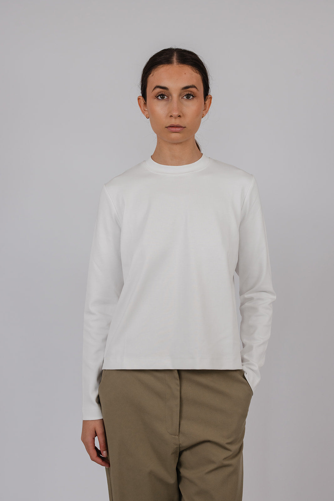 Model wearing a white thick long sleeve tee and green pants by Vic and Bert.